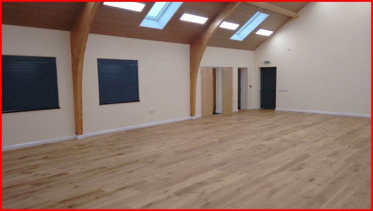 The main hall, looking towards the kitchen serving hatch on the left, with a wooden floor and tall windows.